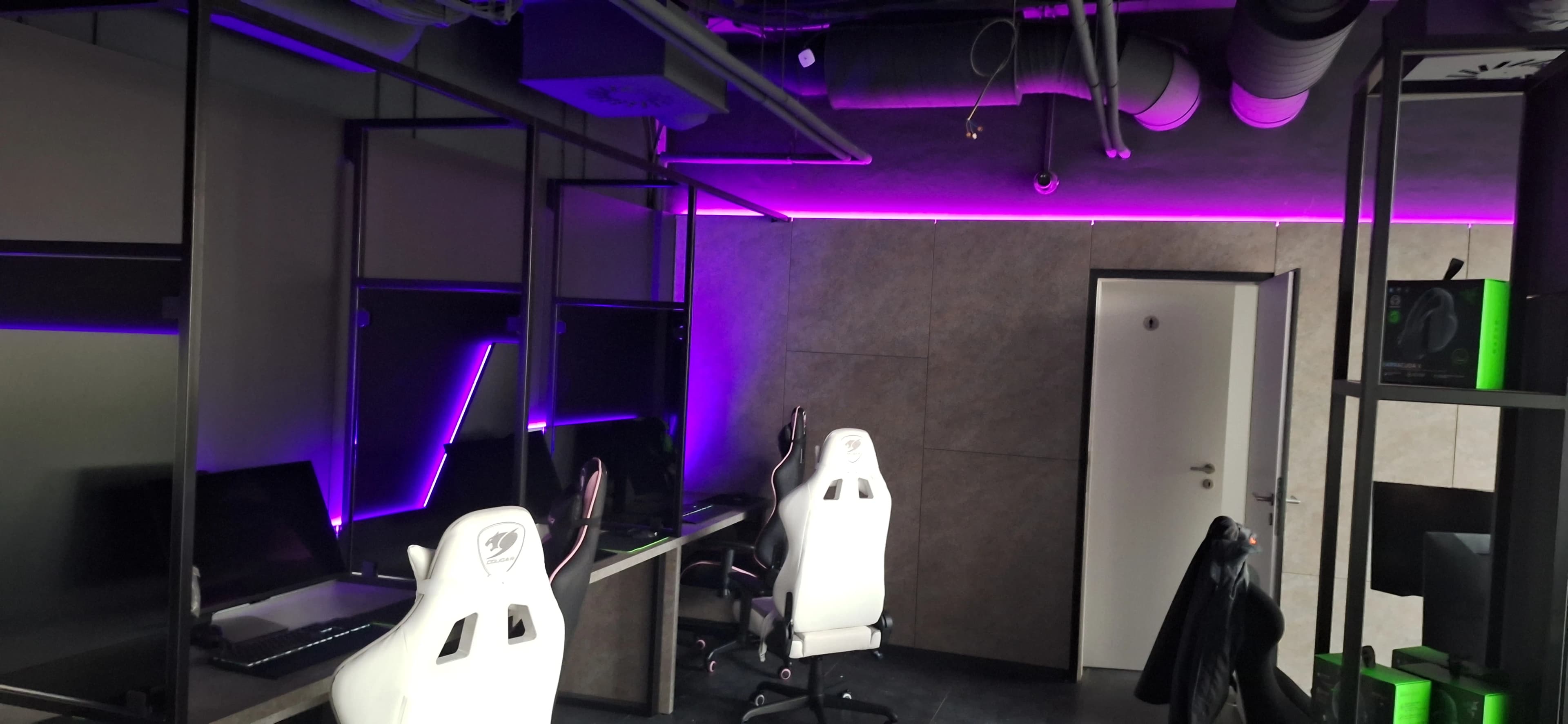 Pohľad na herné stanice s bielymi stoličkami a fialovým LED podsvietením.